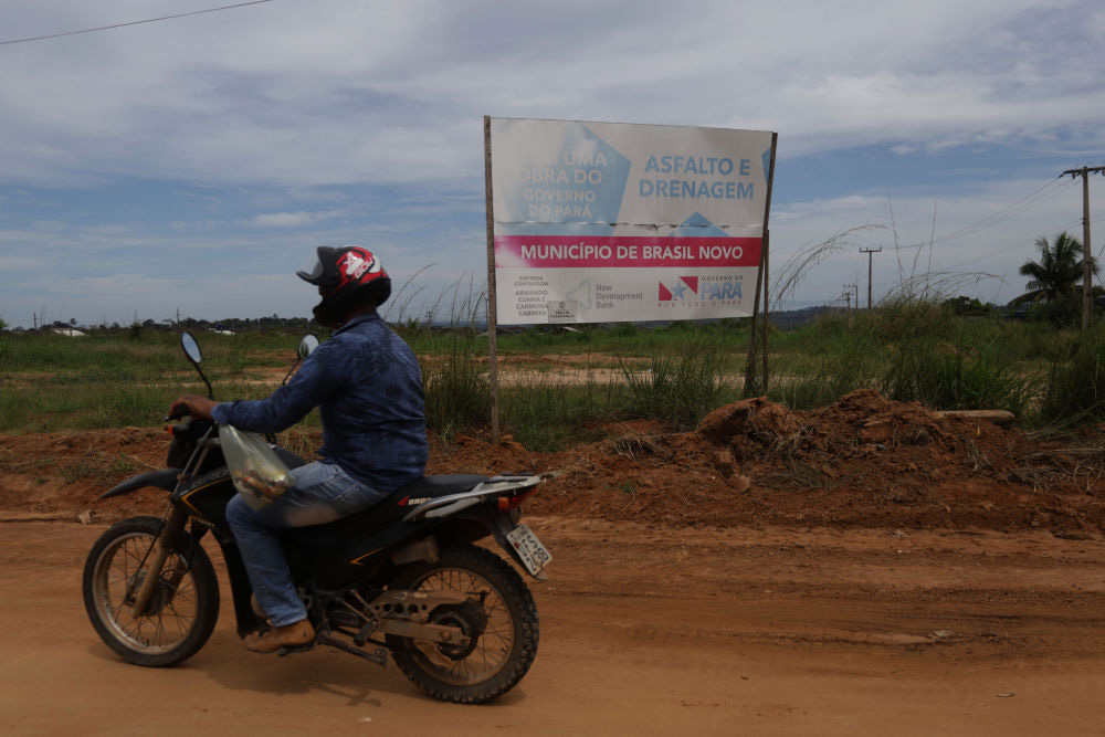 5月19日，在巴西帕拉州巴西诺沃，一名骑摩托车的男子经过一处告示牌。该告示牌显示有金砖国家新开发银行和帕拉州政府字样。