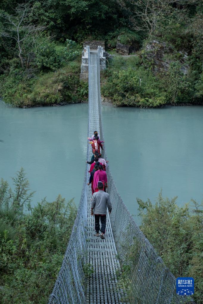 11月8日，在尼泊尔勒姆宗县，村民走过水电站项目公司帮助修缮的吊桥。新华社发（哈里·马哈尔詹摄）